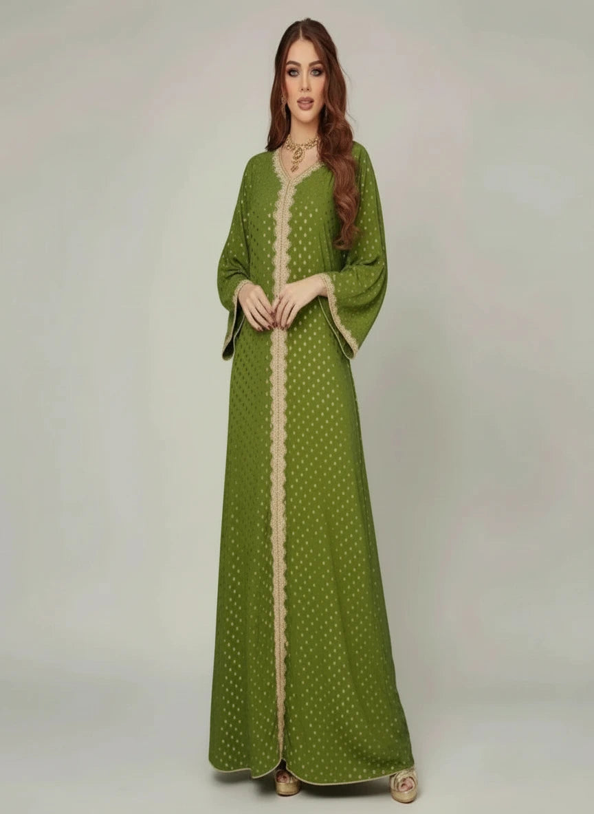 Woman wearing a green dress with white patterns standing indoors next to a plant.