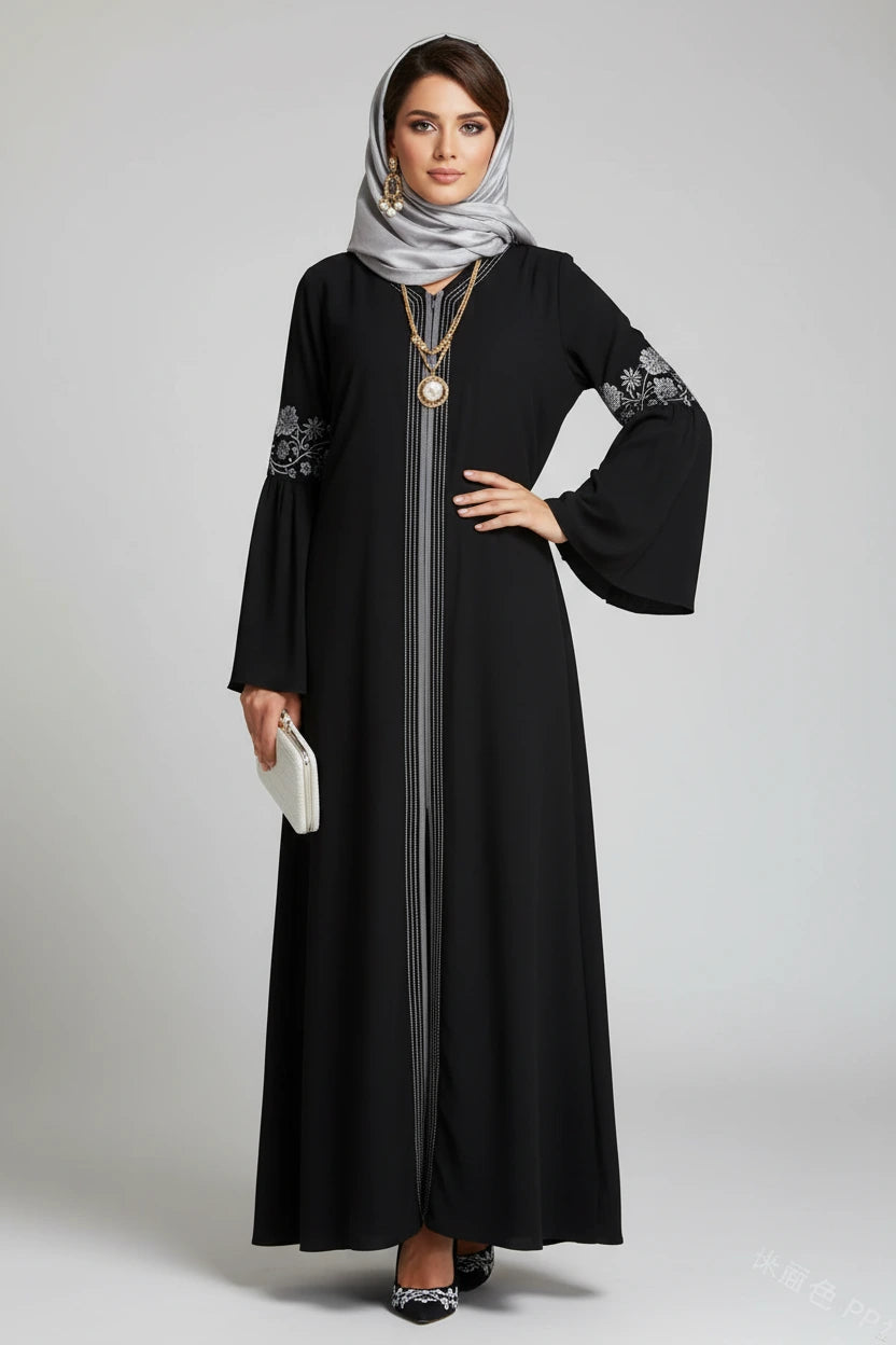 Woman wearing a black abaya with white embroidery on a gray background
