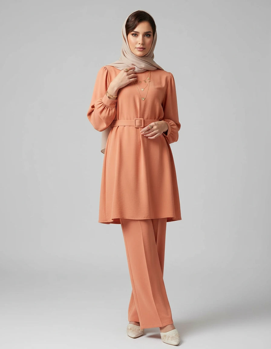 Woman wearing a peach-colored outfit with a hijab on a gray background