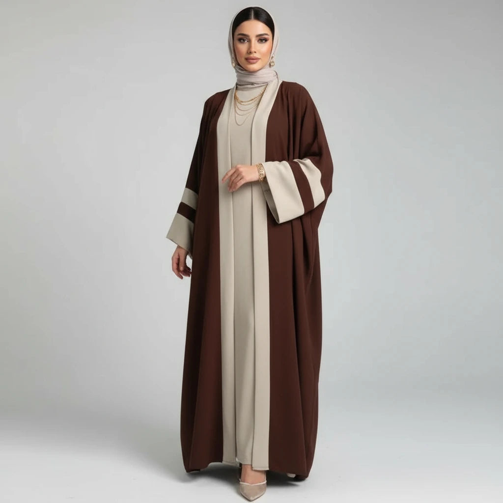 Person wearing a brown and beige abaya standing next to a plant on a white floor.