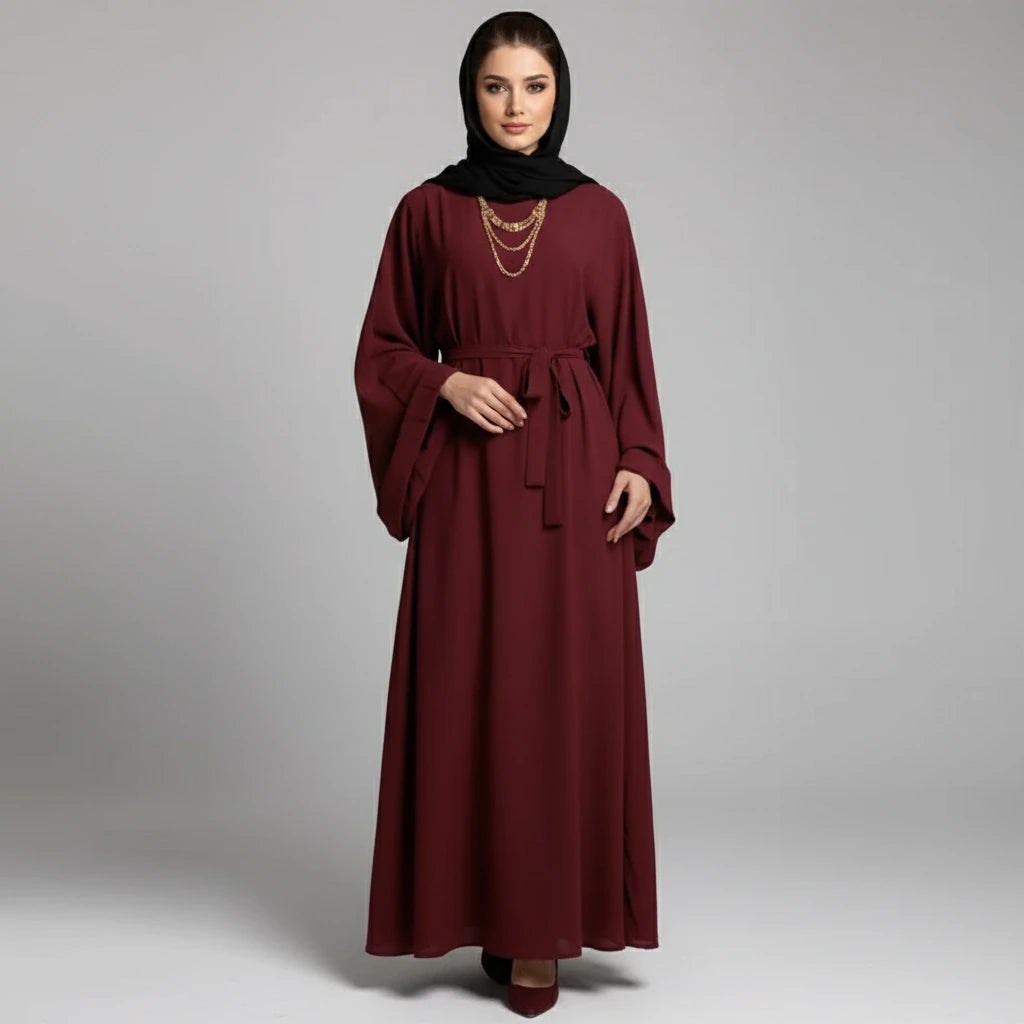 Woman wearing a burgundy dress with wide sleeves on a gray background