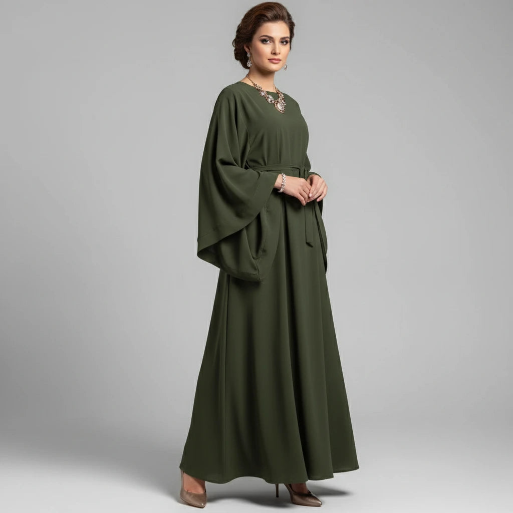 Green abaya worn by a person on a white floor with a chair and decorative vase in the background