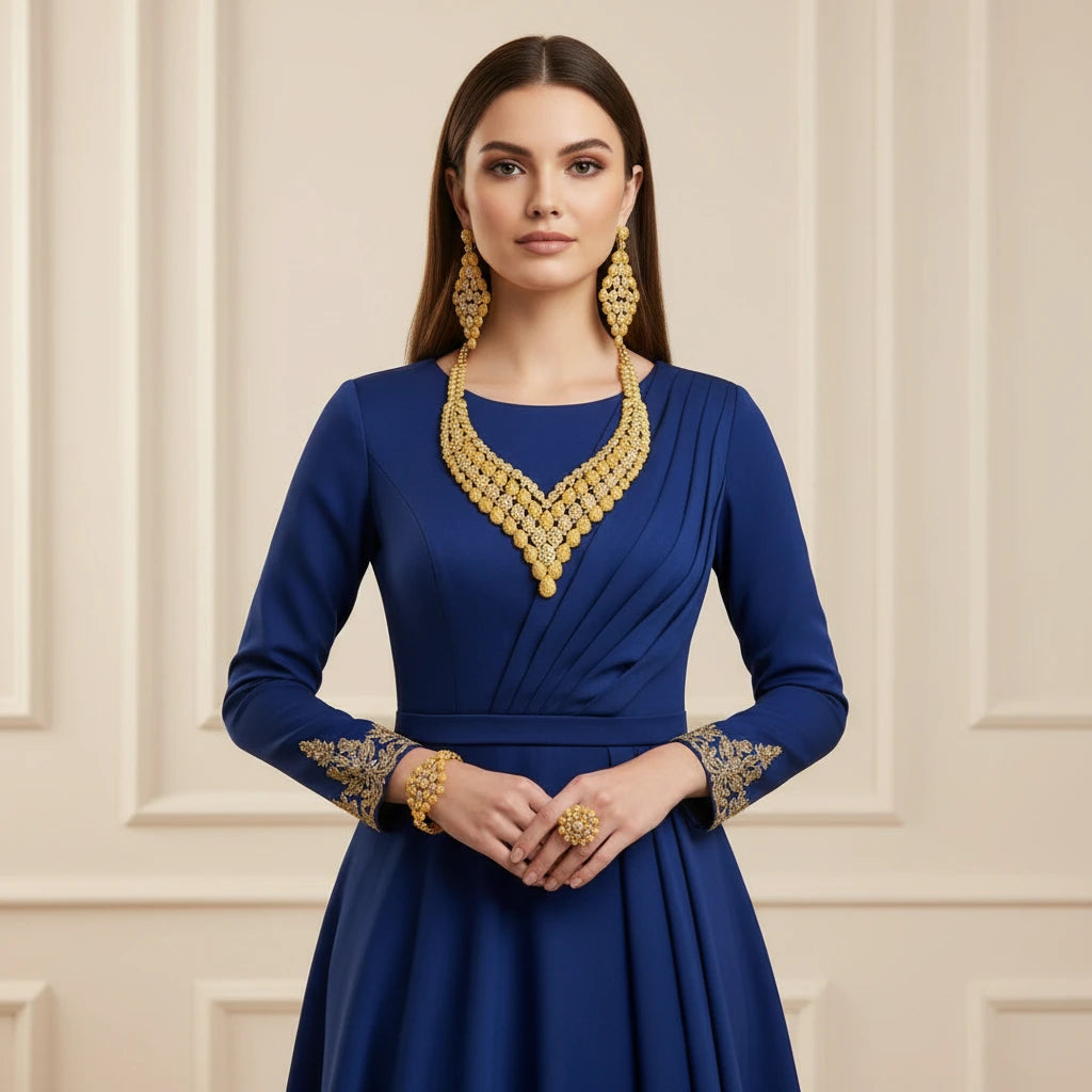 Woman wearing a blue dress with gold detailing and jewelry against a beige wall.