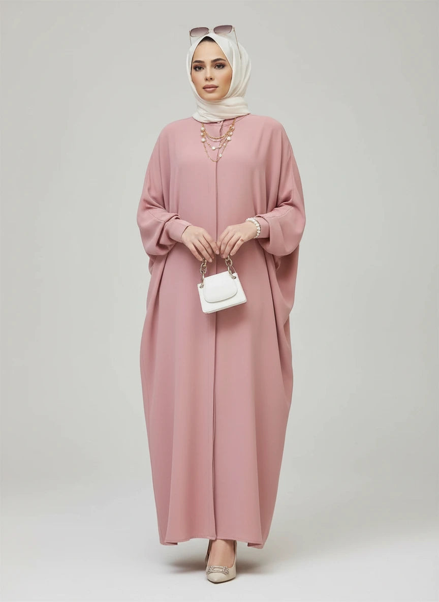 Woman wearing a pink dress with a white hijab in an indoor setting.