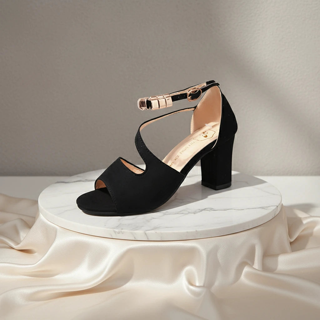 Black sandal with a block heel on a white marble platform with a beige fabric background